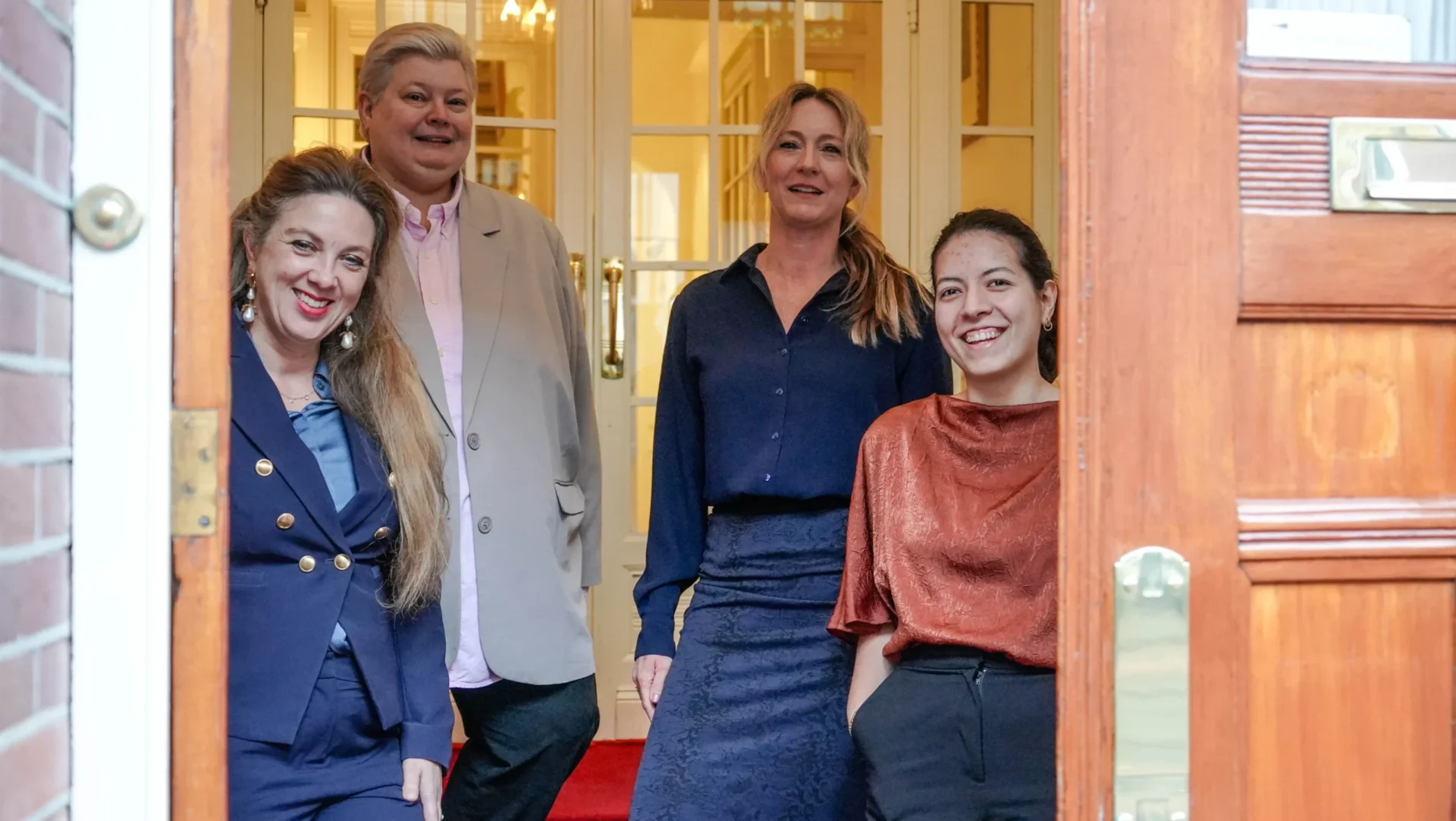 Vier medewerkers staan lachend in de open voordeur van het kantoor