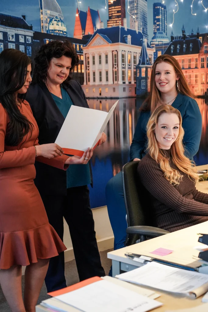 Vijf medewerkers bij een bureau voor een foto van het Haagse Binnenhof en de skyline