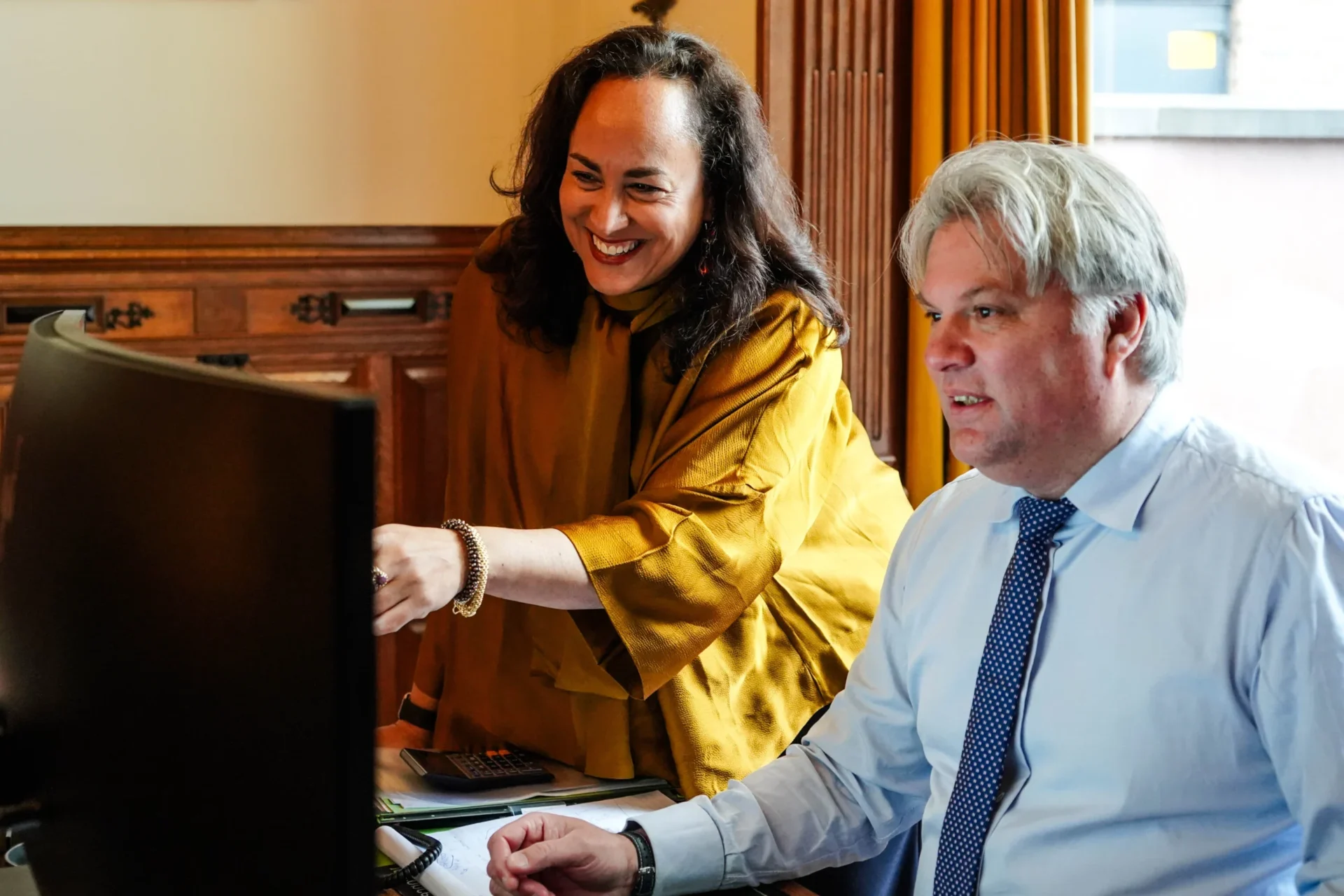 Een vrouw en een man kijken lachend samen naar een computerscherm op kantoor
